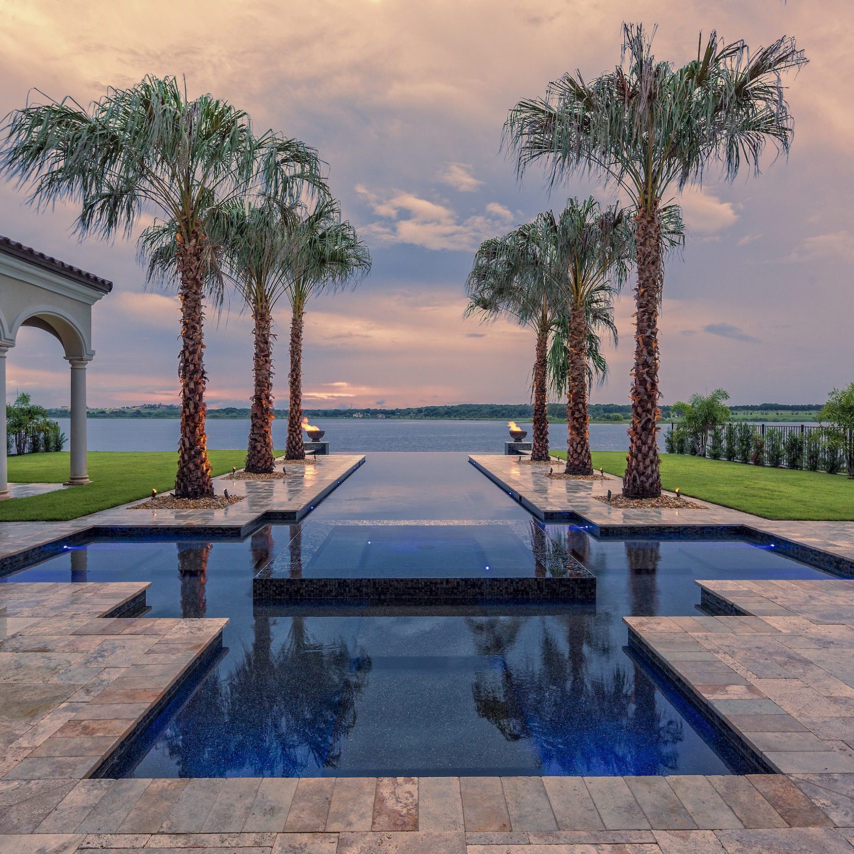 A beautiful estate home with large swimming pool overlooking lake at sunset.